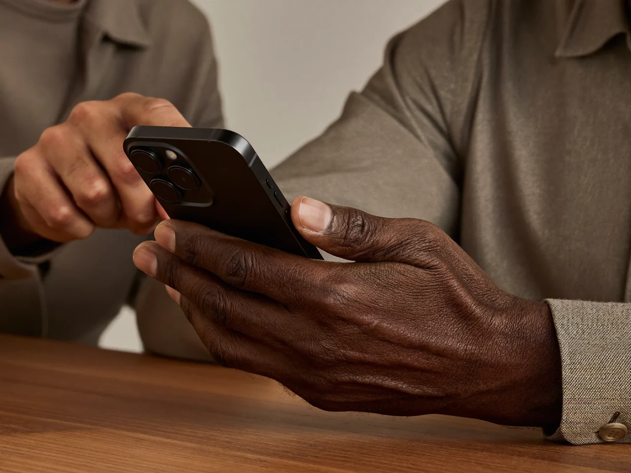 Die Hände eines älteren Mannes am Smartphone, eine Lehrerhand zeigt behutsam auf das Gerät.